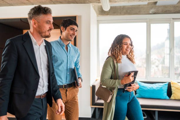 Group of diverse business professionals, including a female and males, in casual professional attire, walking together in a bright modern office setting, engaging in conversation.